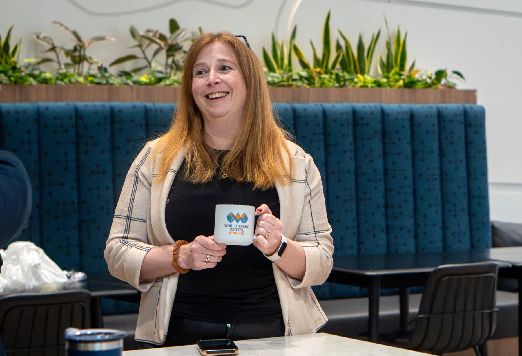 WTC Winnipeg staff member smiling and holding WTC Winnipeg branded mug in the office.
