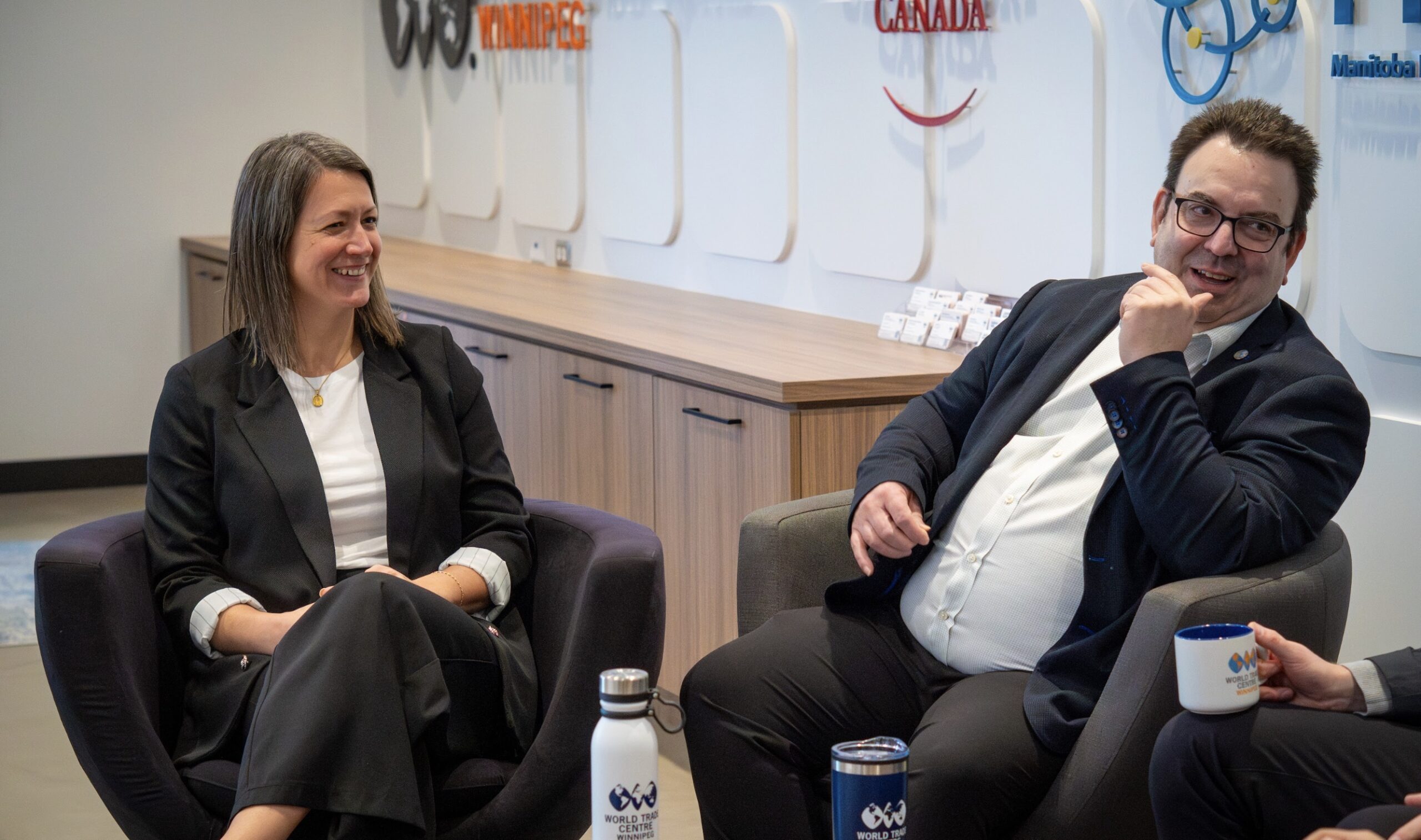 Two World Trade Centre Winnipeg advisors in conversation, seated in armchairs in a branded meeting room