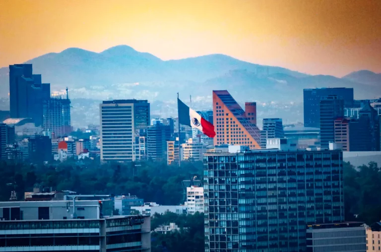 Cityscape of Mexico City with the Mexican flag and mountains at sunset.