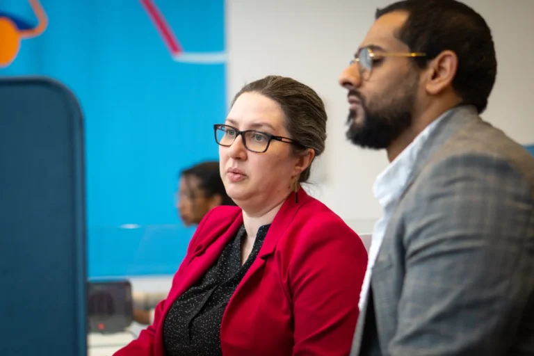Two business professionals, a woman in a red blazer and a man in a grey suit, engaged in discussion, representing business planning and preparation for international market expansion.